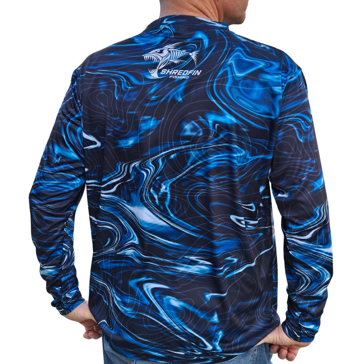 ShredFin StormSurge Performance Shirt in Blue Abyss, shown in a minimalist living room setting, highlighting its sleek design and fabric.
