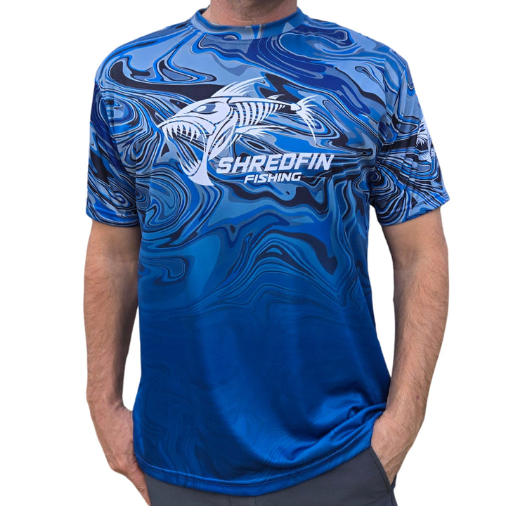 ShredFin StormSuge short sleeve performance shirt in blue harbor swirl, displayed in a minimalist living room setting.